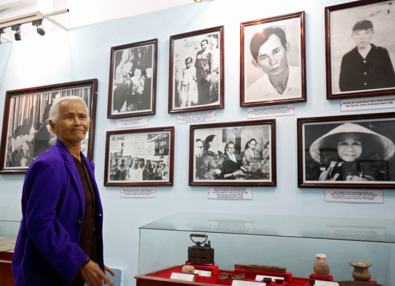 Pham Thi Thuan, My Lai massacre survivor, stands in front of photographs of her and other survivors exhibited at a museum during the 50th anniversary of the My Lai massacre in My Lai village