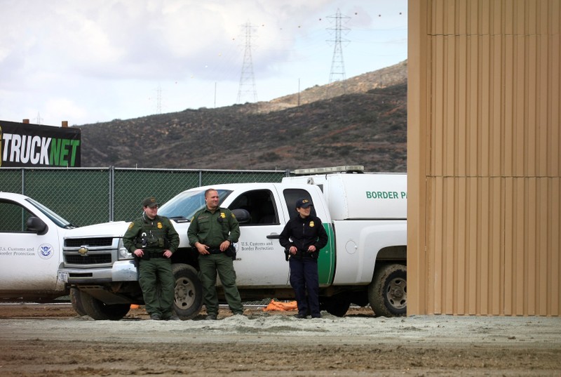 U.S. border patrol officers are pictured near a prototype for U.S. President Donald Trump's border wall with Mexico, behind the current border fence