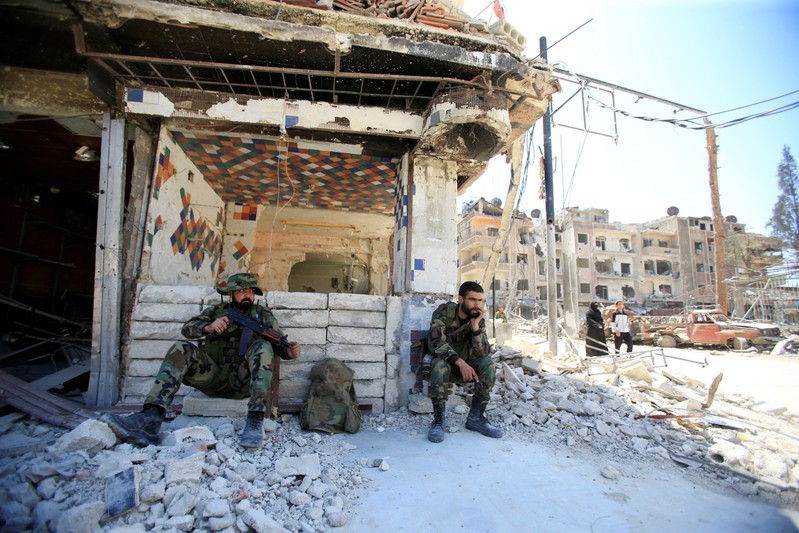 Members of Syrian police sit at a damaged building at the city of Douma, Damascus