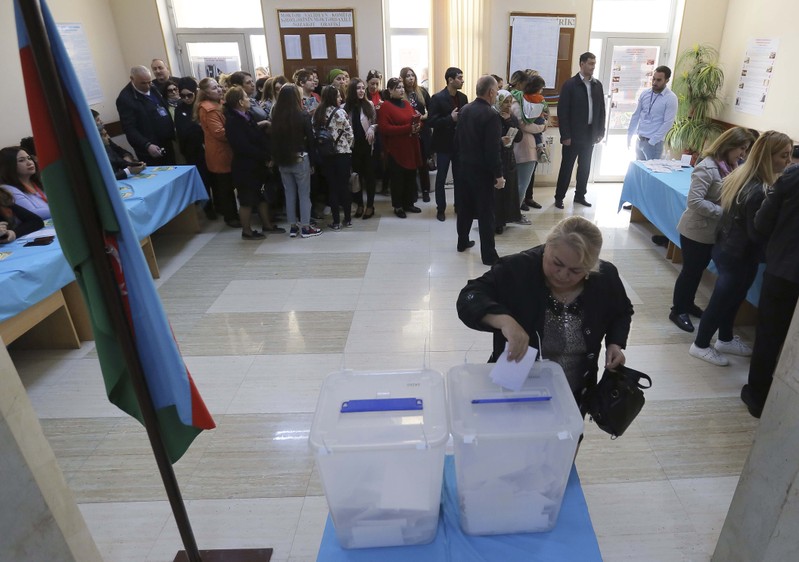 A woman casts her ballot as people queue to vote during the presidential election at a polling station in Baku