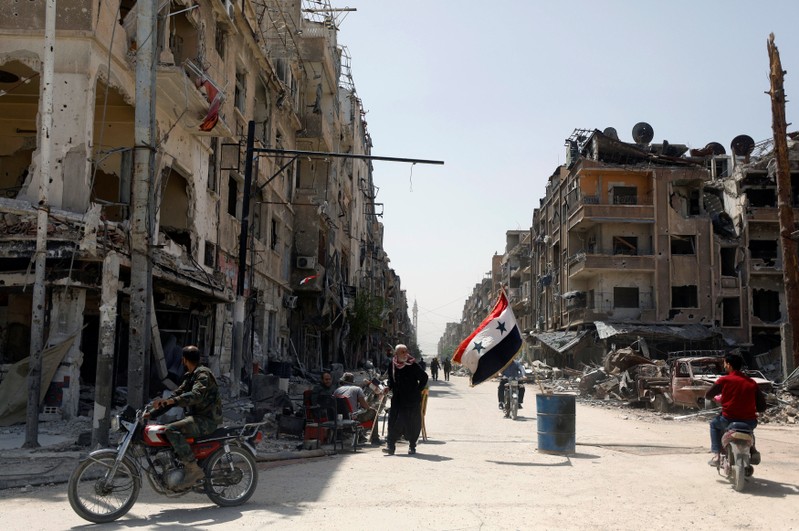 A Syrian flag flutters along a damaged street at the city of Douma in Damascus