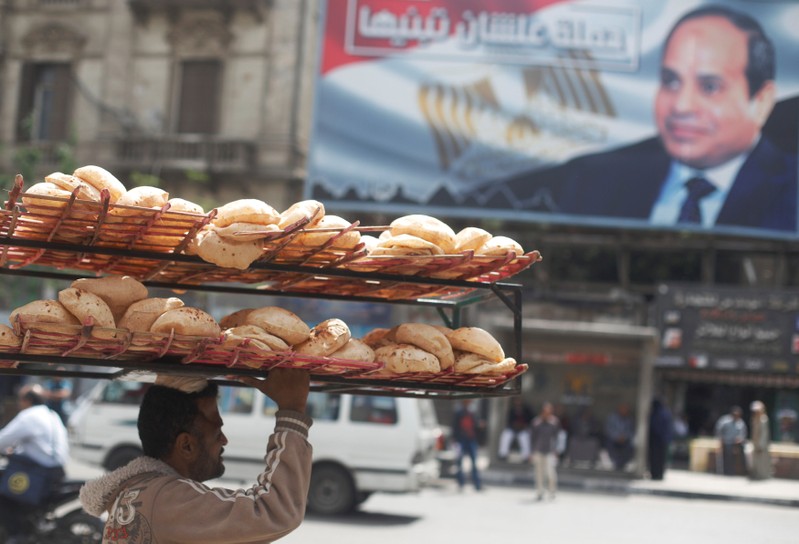 A man carries breads on his head along a busy street near a banner for Egypt's President Abdel Fattah al-Sisi after election results in Cairo