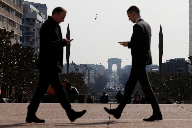 Men look at their mobile phones as they walk on the esplanade of La Defense in the financial and business district of La Defense, west of Paris