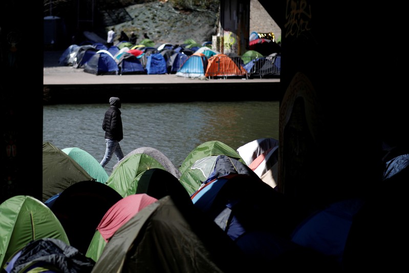 A migrant walks by the tents in a makeshift camp along the Canal Saint-Denis in Paris
