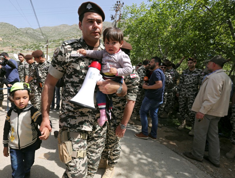 Lebanese general security member holds Syrian refugee children, who fled to Lebanon, as they wait for buses to go back to Syria from the southern village of Shebaa