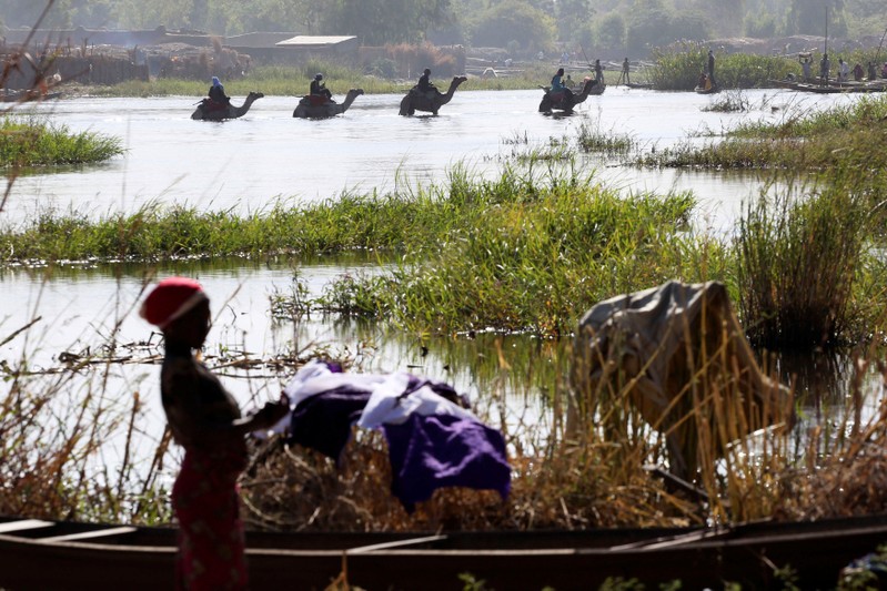 FILE PHOTO: Men on camels cross the water as a woman washes clothes in Lake Chad in Ngouboua