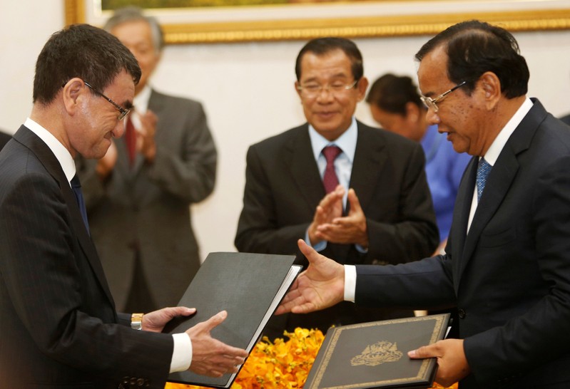 Japan's Foreign Minister Taro Kono exchanges a document with his Cambodia's counterpart Prak Sokhonn as Cambodia's Prime Minister Hun Sen applauds after a signing ceremony in Phnom Penh