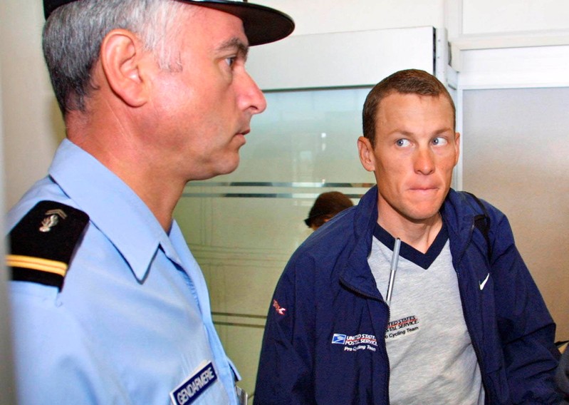 FILE PHOTO: US Postal Service team leader Lance Armstrong of the USA looking at a French gendarme before boarding for the transfer stage of the Tour de France cycling race