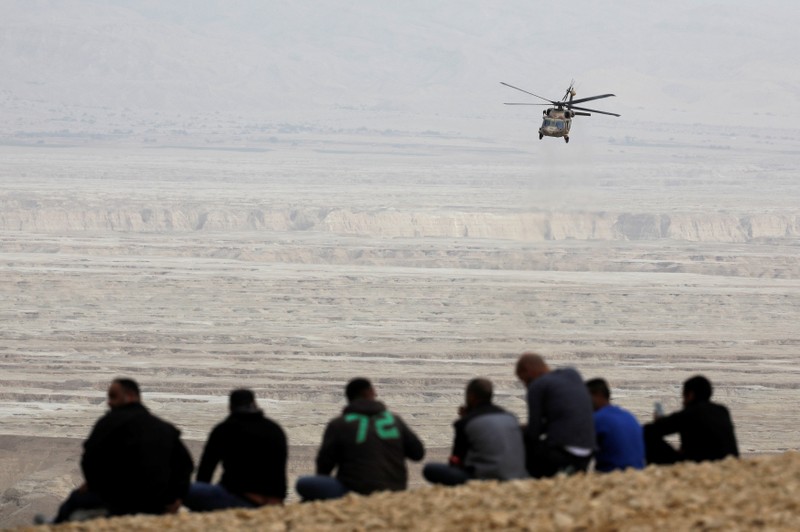 People look on as Israeli rescue services helicopter operates near the site where a group of Israeli youths was swept away by a flash flood, near the Zafit river bed, south to the Dead Sea