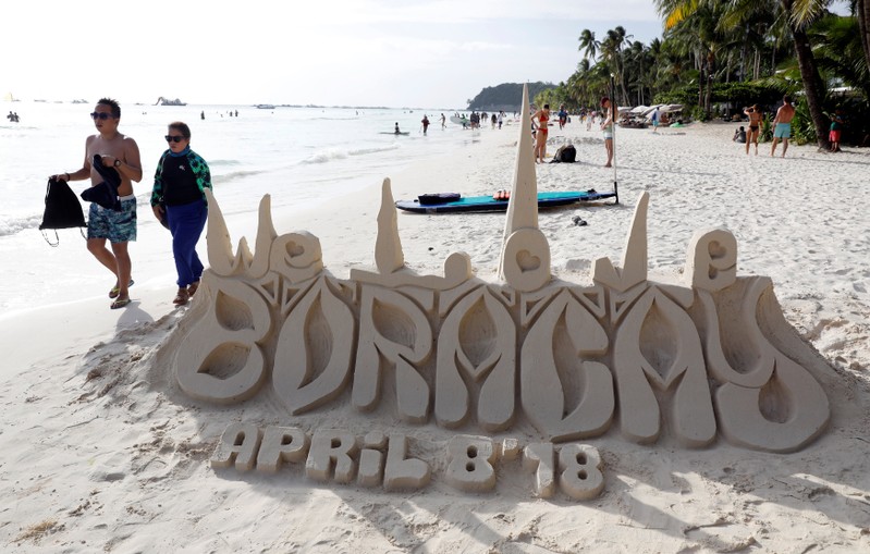 Tourists walk near a sand sculpture along the beach of Boracay