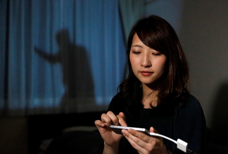 Leopalace 21 Corp employee, Mai Shibata, poses with her mobile phone during a demonstartion of the company's security system 'Man on the Curtain' in her room in Tokyo