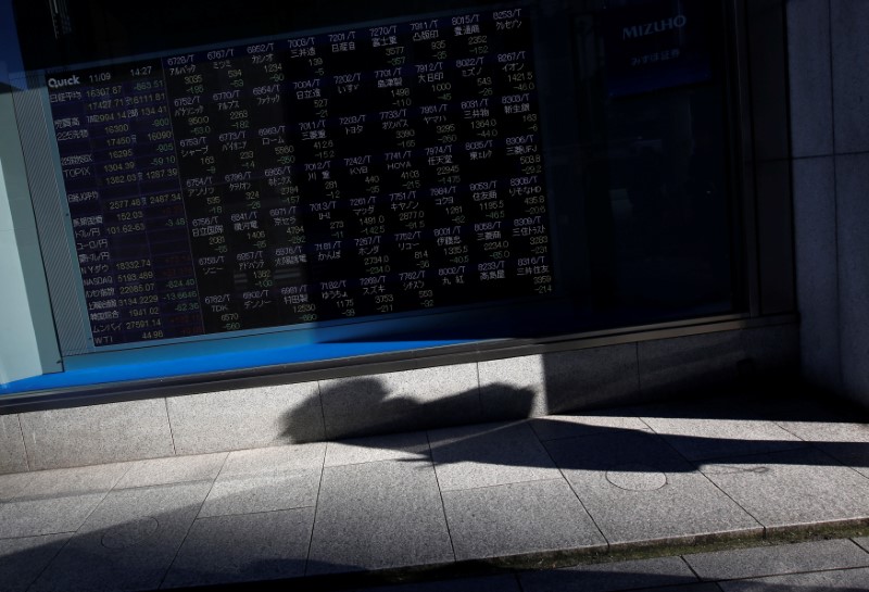 A pedestrian casts a shadow in front of an electronic stock quotation board outside a brokerage in Tokyo, Japan