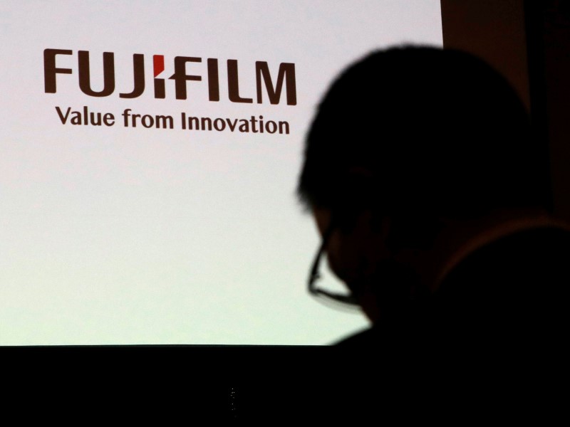 A man is silhouetted in front of Fujifilm Holdings' logo ahead of its news conference in Tokyo