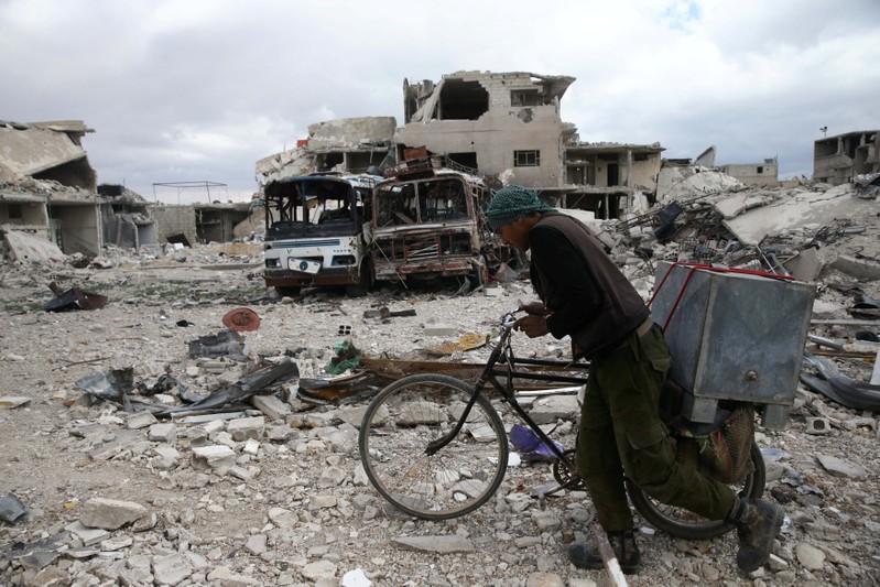 A man walks with his bicycle at a damaged site in the besieged town of Douma