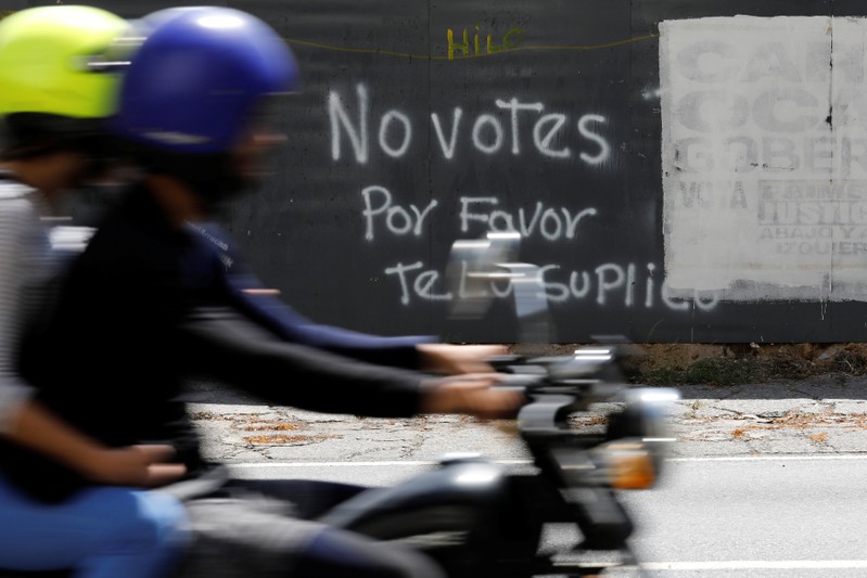 A motorcycle passes graffiti painted on a fence in Caracas