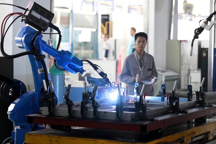 FILE PHOTO: Worker monitors a robotic arm working inside a factory in Huaian