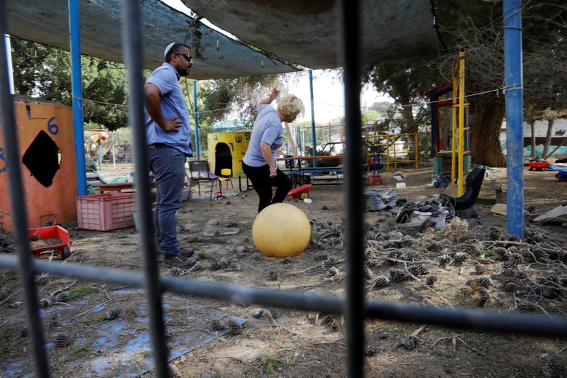 People stand in a kindergarten yard damaged by mortar shells fired from the Gaza Strip that landed near it, in a Kibbutz on the Israeli side of the Israeli-Gaza border