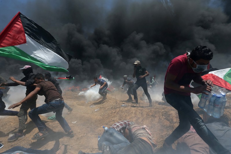Palestinian demonstrators run for cover from Israeli fire and tear gas during a protest against U.S. embassy move to Jerusalem and ahead of the 70th anniversary of Nakba, at the Israel-Gaza border in the southern Gaza Strip