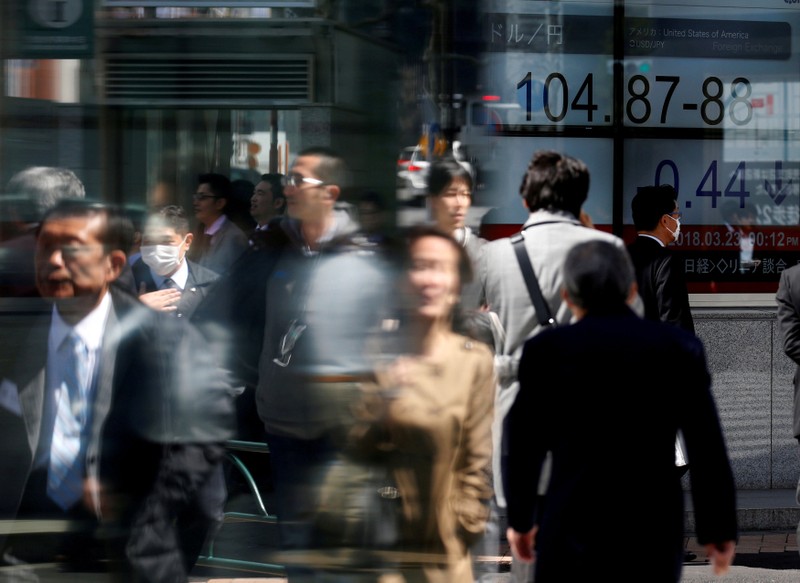 FILE PHOTO: People walk past an electronic board showing exchange rate between Japanese Yen and U.S. Dollar outside a brokerage at a business district in Tokyo