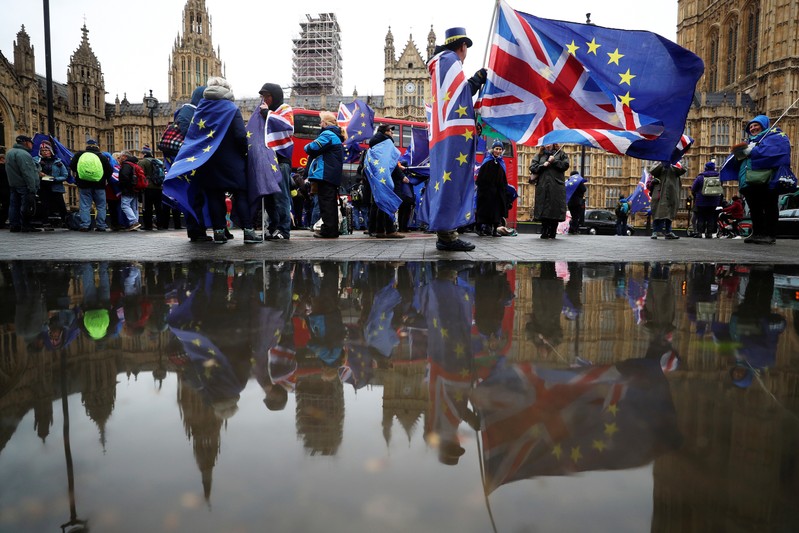 Anti-Brexit protesters are reflected in a puddle as they demonstrate opposite the Houses of Parliament in London