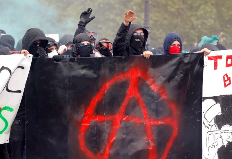 Masked and hooded protesters react as they walk behind a banner during the traditional May Day labour union march in Paris