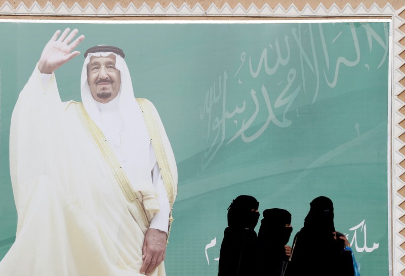 FILE PHOTO: Women walk past a poster of Saudi Arabia's King Salman bin Abdulaziz Al Saud during Janadriyah Cultural Festival on the outskirts of Riyadh