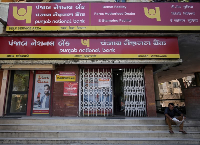 FILE PHOTO: A man reads a newspaper outside a branch of Punjab National Bank in Ahmedabad