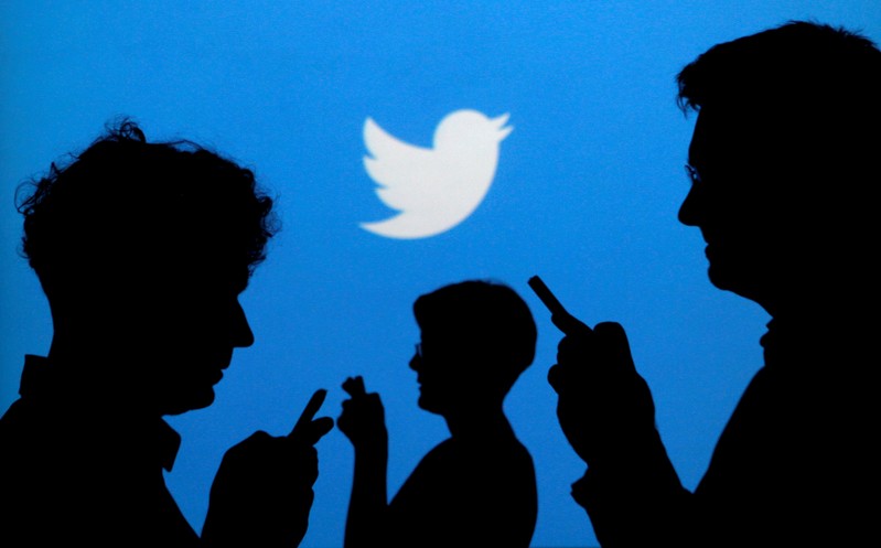 FILE PHOTO - People holding mobile phones are silhouetted against a backdrop projected with the Twitter logo in Warsaw