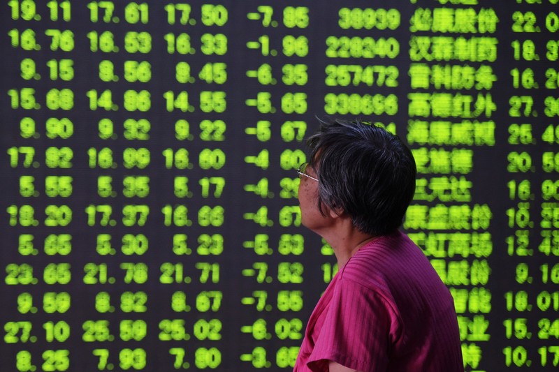 Woman looks at an electronic board showing stock information at a brokerage house in Hangzhou