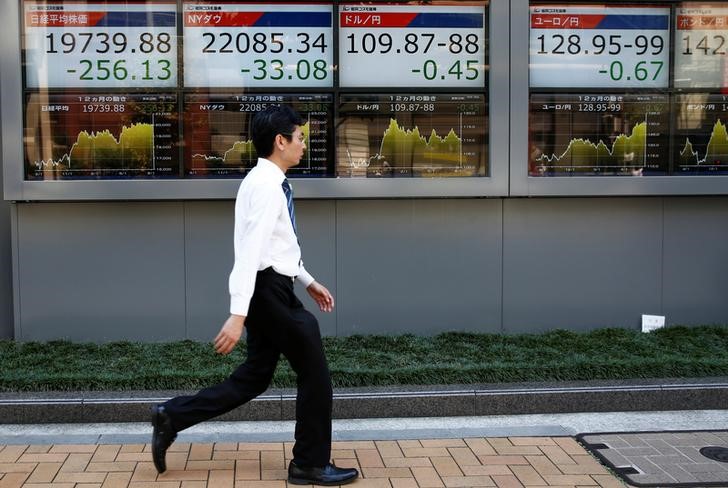 FILE PHOTO: A man walks past electronic boards showing Japan's Nikkei average, the Dow Jones Industrial Average and foreign exchange rates outside a brokerage at a business district in Tokyo