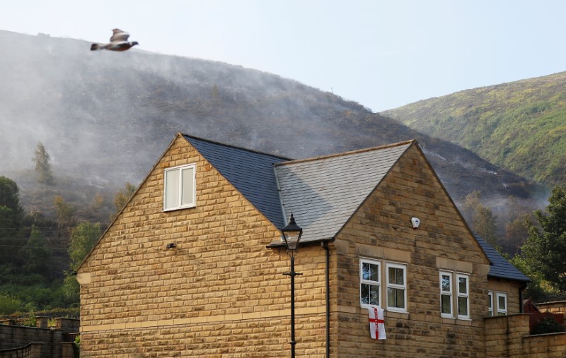 A fire smoulders behind evacuated homes on a moor above Carrwood