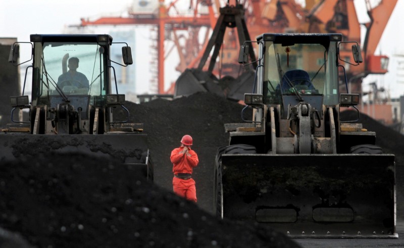 FILE PHOTO - An employee walks between front-end loaders which are used to move coal imported from North Korea at Dandong port in the Chinese border city of Dandong