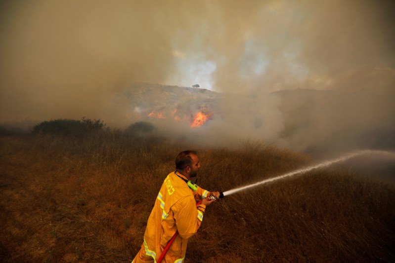 A firefighter attempts to extinguish a fire burning scrubland in an area where Palestinians have been causing blazes by flying kites and balloons loaded with flammable materials, on the Israeli side of the border between Israel and the Gaza Strip, near kib