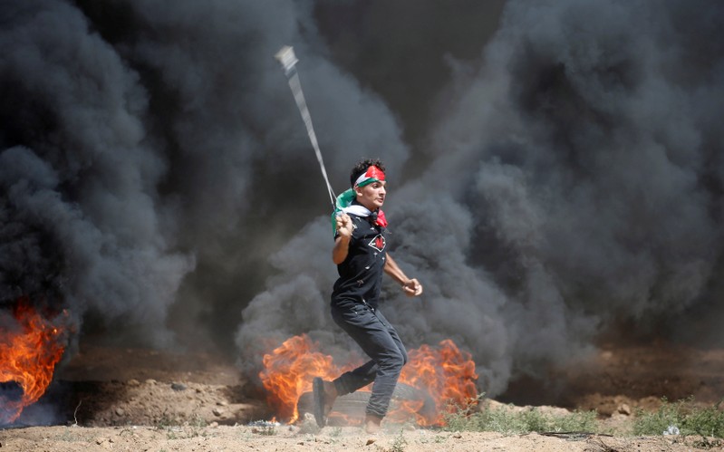 Palestinian demonstrator uses a sling to hurl stones at Israeli troops during a protest marking al-Quds Day, (Jerusalem Day), at the Israel-Gaza border, east of Gaza City