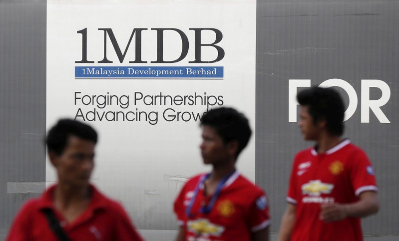 FILE PHOTO: Men walk past a 1 Malaysia Development Berhad (1MDB) billboard at the fund's flagship Tun Razak Exchange development in Kuala Lumpur