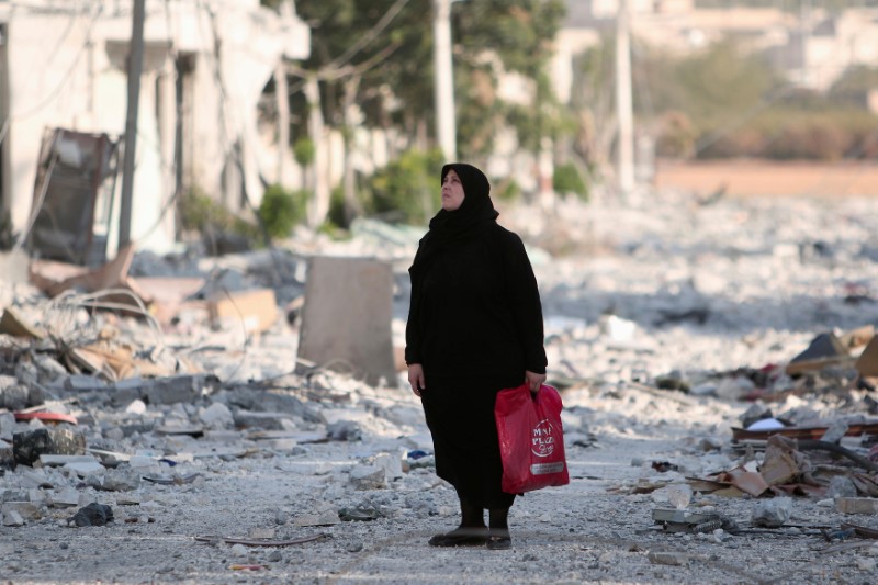 A woman stands along a damaged street in Manbij, Aleppo Governorate