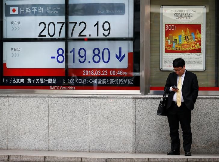 Man looks at a mobile phone next to an electronic board showing Japan's Nikkei average outside a brokerage in Tokyo