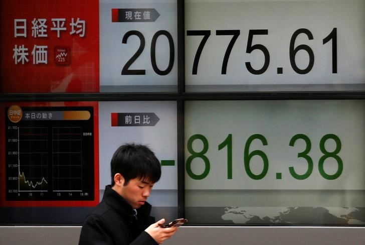 Man looks at a mobile phone in front of an electronic board showing Japan's Nikkei average outside a brokerage in Tokyo