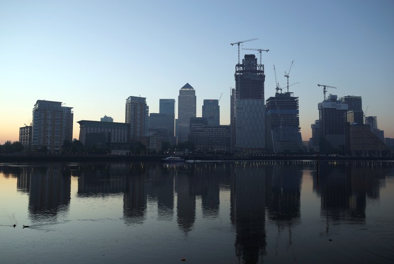 The Canary Wharf financial district is reflected in the river Thames on a sunny morning in London