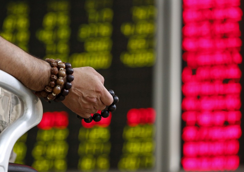 FILE PHOTO: An investor holds onto prayer beads as he watches a board showing stock prices at a brokerage office in Beijing