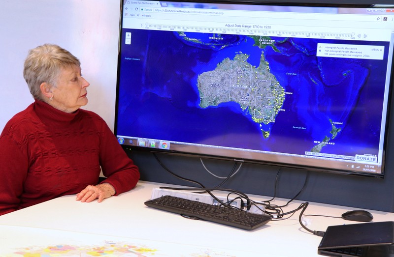 A supplied image shows University of Newcastle research academic, Professor Lyndall Ryan, sitting in front of a screen displaying a map detailing the number of Aboriginal and Torres Strait Islander massacres that occurred on Australia’s colonial frontier