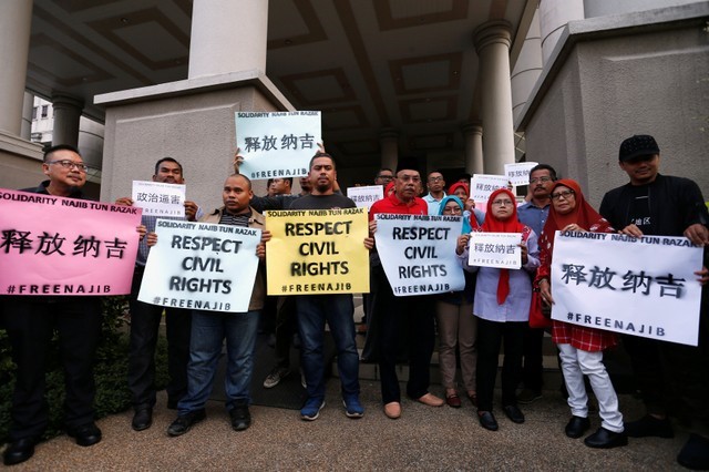 Supporters of former Malaysian prime minister Najib Razak hold up signs, ahead of his arrival to court in Kuala Lumpur