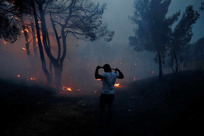 A man uses a cloth to protect himself from smoke as wildfire burns in the town of Rafina, near Athens