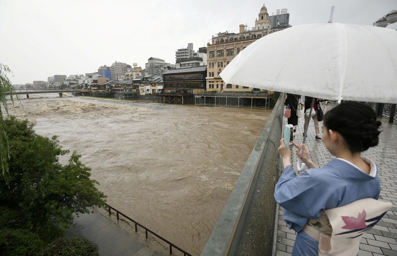 A kimono-clad woman using a smartphone takes photos of swollen Kamo River caused by a heavy rain from Shijo Bridge in Kyoto