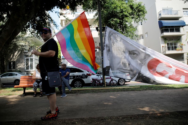 A man holds a flag next to a banner with the photo of Israeli Prime Minister Benjamin Netanyahu, during a LGBT community members protest against discriminatory surrogate bill in Tel Aviv