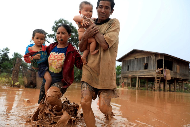 Parents carry their children as they leave their home during the flood after the Xepian-Xe Nam Noy hydropower dam collapsed in Attapeu province