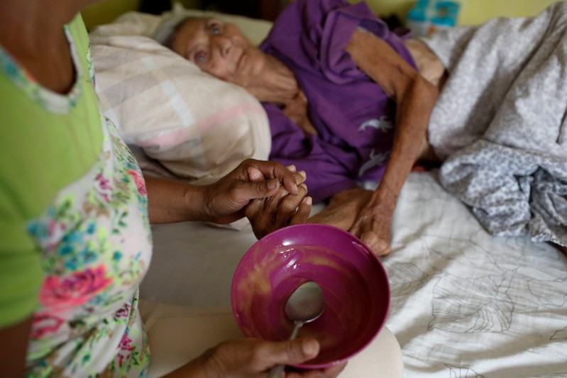 Judith Palmar holds her mother Sibilina Caro hand after feeding her at their home in Maracaibo