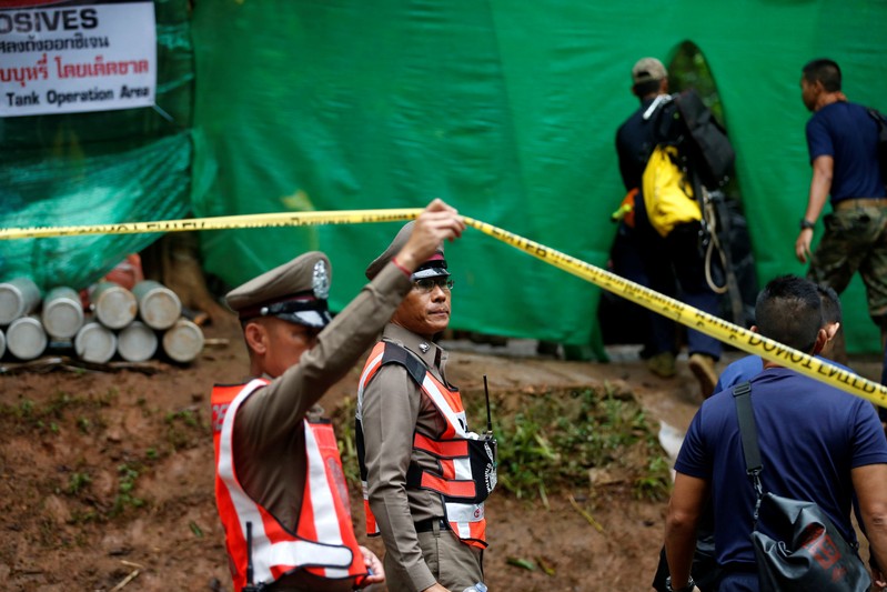 Police officer raises a police tape as divers arrive at the Tham Luang cave complex after Thailand's government instructed members of the media to move out urgently, in the northern province of Chiang Rai