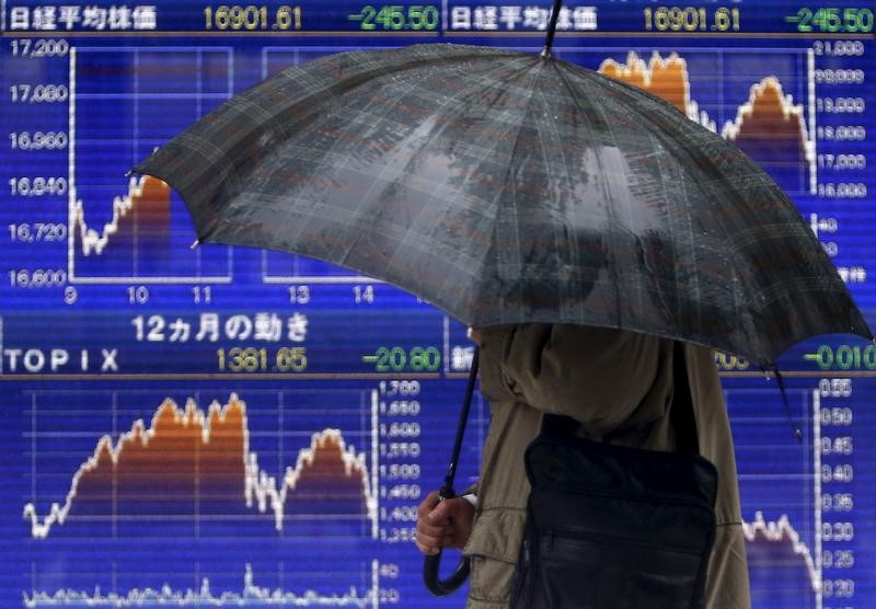 FILE PHOTO: A pedestrian holding an umbrella walks past an electronic board showing the graphs of the recent fluctuations of Japan's Nikkei average outside a brokerage in Tokyo