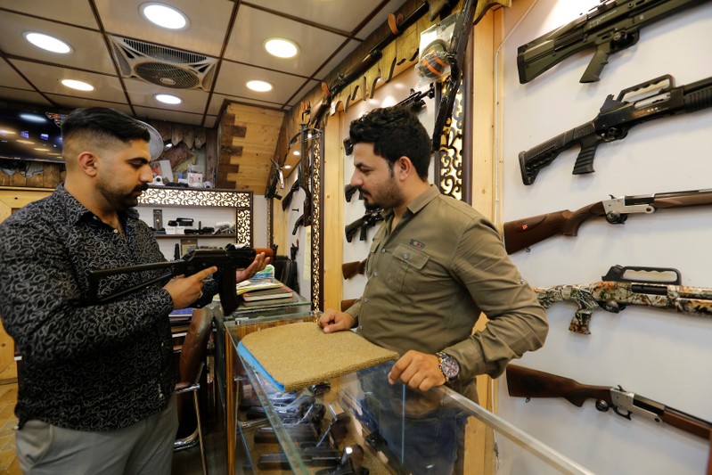 A man checks a weapon before he buys at a weapons shop in Baghdad